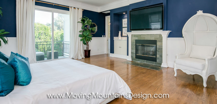 Idée de décoration pour une grande chambre parentale design avec un mur bleu, un sol en bois brun, une cheminée standard et un manteau de cheminée en pierre.