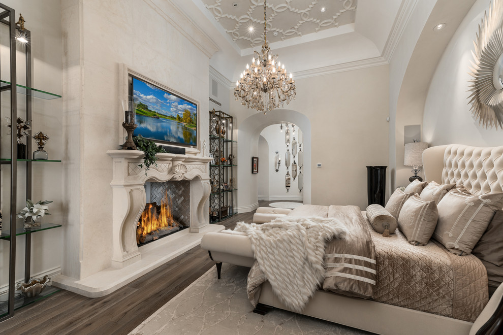 Expansive modern master bedroom in Phoenix with white walls, dark hardwood flooring, a two-sided fireplace, a stone fireplace surround and brown floors.