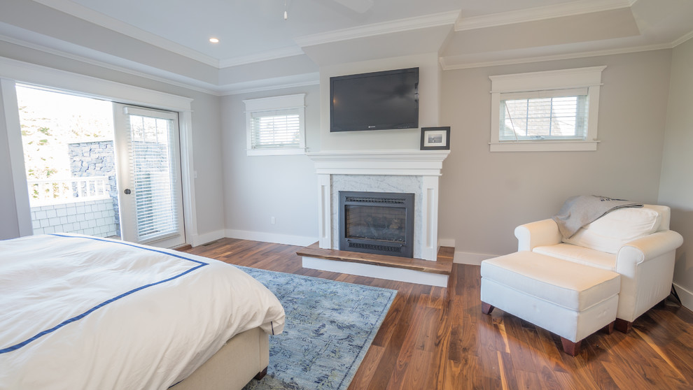 Imagen de dormitorio principal de estilo americano grande con paredes grises, suelo de madera en tonos medios, todas las chimeneas y marco de chimenea de madera