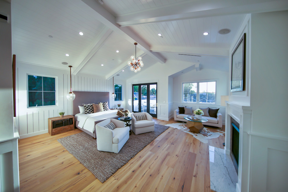 Großes Maritimes Hauptschlafzimmer mit weißer Wandfarbe, hellem Holzboden, Kamin, Kaminumrandung aus Holz und braunem Boden in Los Angeles