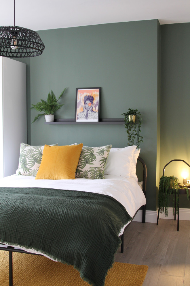 Modelo de habitación de invitados minimalista de tamaño medio sin chimenea con paredes verdes, suelo laminado y suelo marrón