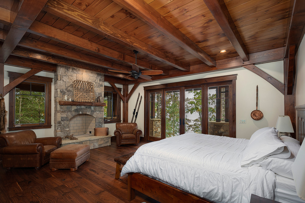 Uriges Schlafzimmer mit weißer Wandfarbe, braunem Holzboden, Kamin, Kaminumrandung aus Stein und braunem Boden in Sonstige