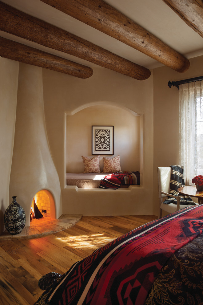 Southwest guest medium tone wood floor bedroom photo in Albuquerque with beige walls, a plaster fireplace and a standard fireplace