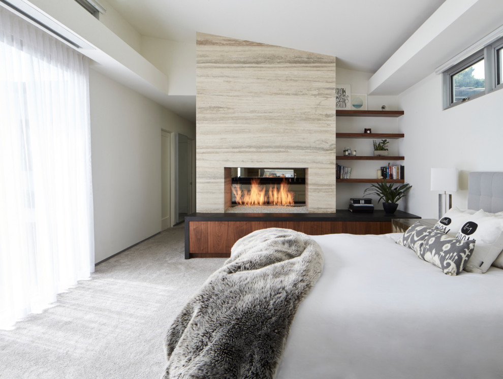 Diseño de dormitorio principal minimalista con moqueta, chimenea de doble cara, marco de chimenea de piedra y suelo gris