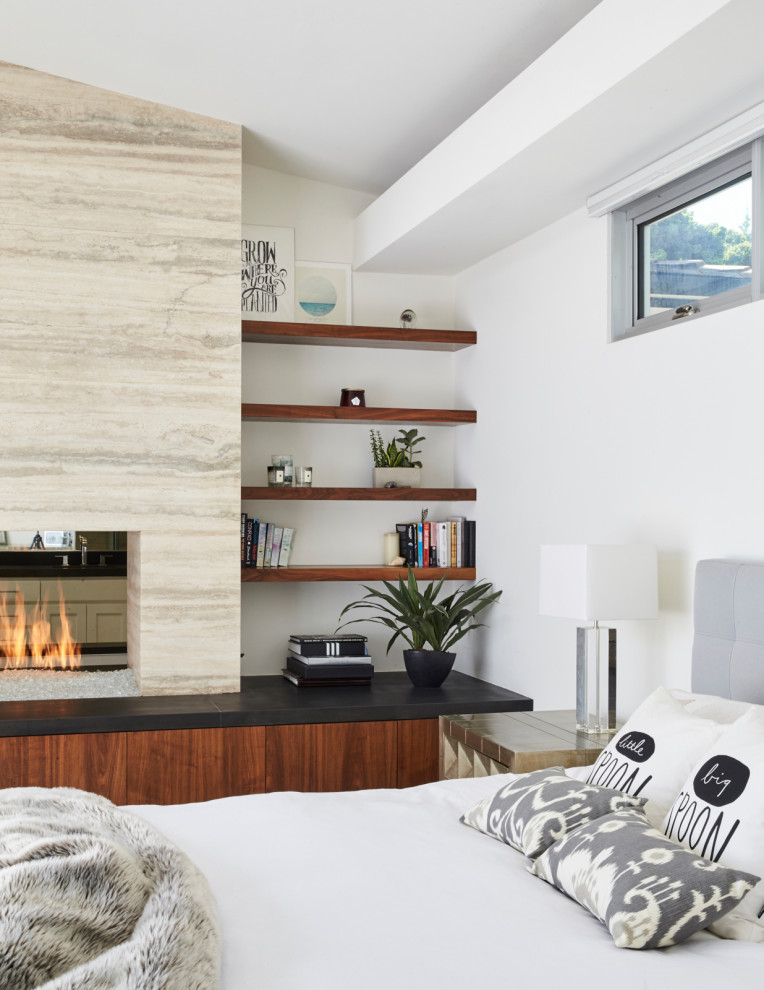 На фото: хозяйская спальня в стиле модернизм с ковровым покрытием, двусторонним камином, фасадом камина из камня и серым полом
