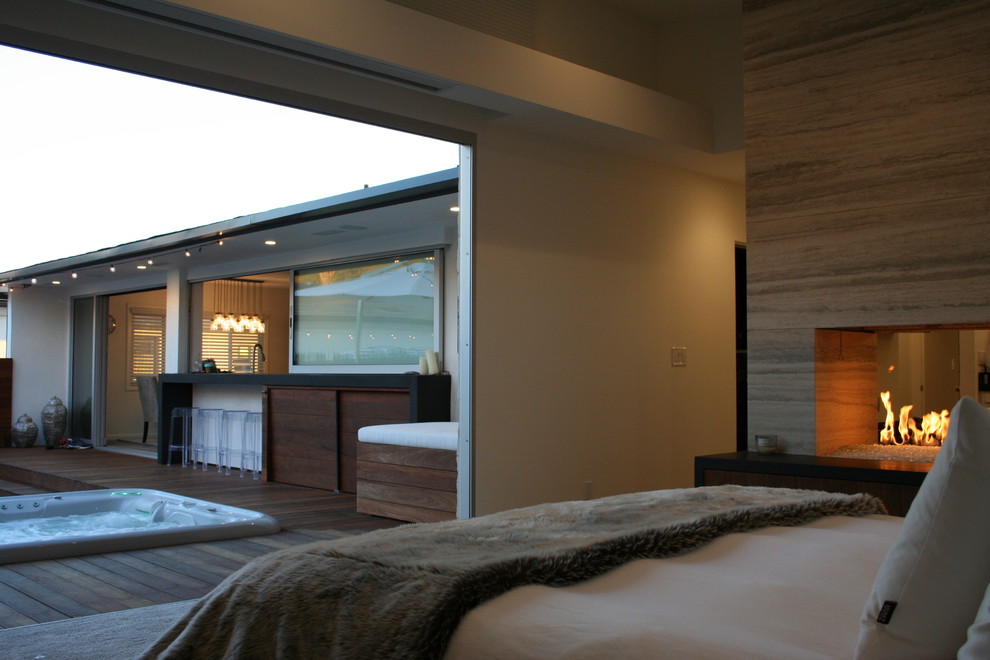Modelo de dormitorio principal moderno con moqueta, chimenea de doble cara y marco de chimenea de piedra