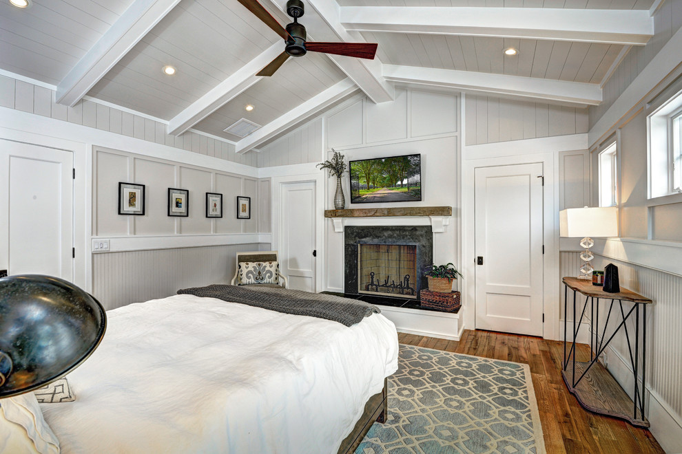 Cette photo montre une chambre parentale bord de mer de taille moyenne avec un mur gris, un sol en bois brun, une cheminée standard et un manteau de cheminée en pierre.