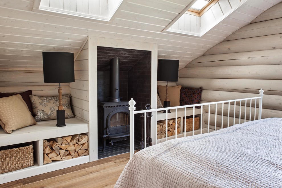 Imagen de dormitorio de estilo de casa de campo con estufa de leña, suelo de madera clara y techo inclinado