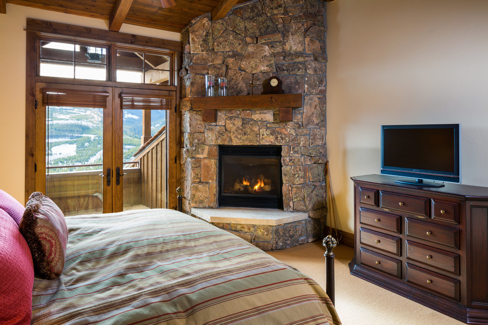 Ejemplo de dormitorio principal rústico grande con paredes beige, moqueta, chimenea de esquina y marco de chimenea de piedra