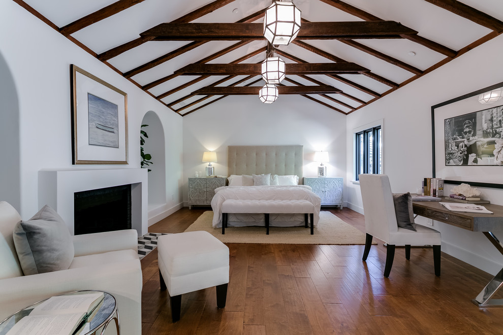 Exemple d'une chambre parentale chic de taille moyenne avec un mur blanc, un sol en bois brun, une cheminée standard, un manteau de cheminée en plâtre et un sol marron.