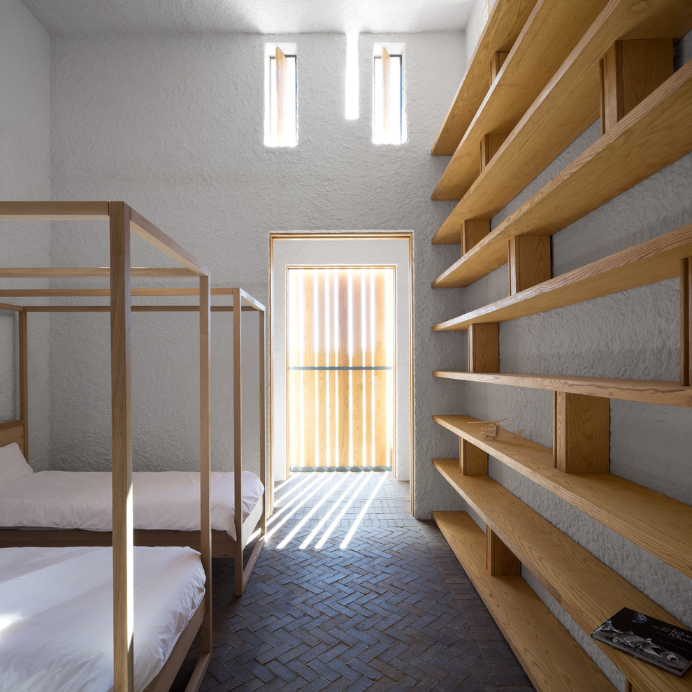 На фото: гостевая спальня (комната для гостей) в современном стиле с белыми стенами и кирпичным полом