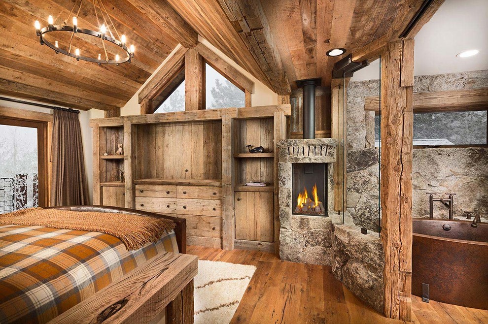 Idées déco pour une grande chambre parentale montagne avec un mur beige, un sol en bois brun, un poêle à bois et un manteau de cheminée en pierre.