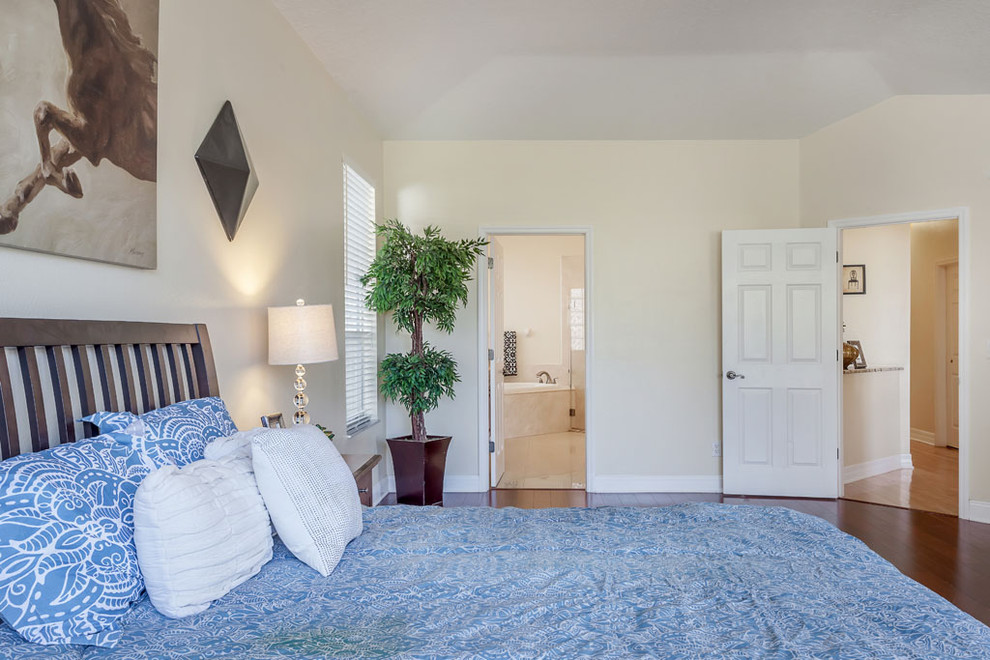 Cette image montre une grande chambre parentale traditionnelle avec un mur beige et un sol en bois brun.