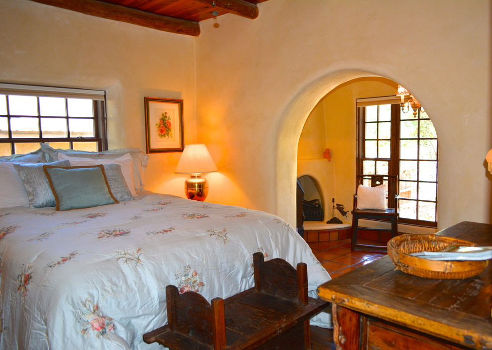 Exemple d'une grande chambre d'amis méditerranéenne avec un mur beige, tomettes au sol, une cheminée d'angle et un manteau de cheminée en plâtre.