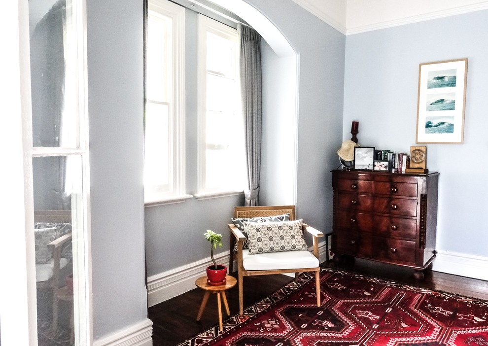 Modelo de habitación de invitados de estilo de casa de campo de tamaño medio con paredes azules, suelo de madera en tonos medios, chimenea de esquina y marco de chimenea de piedra