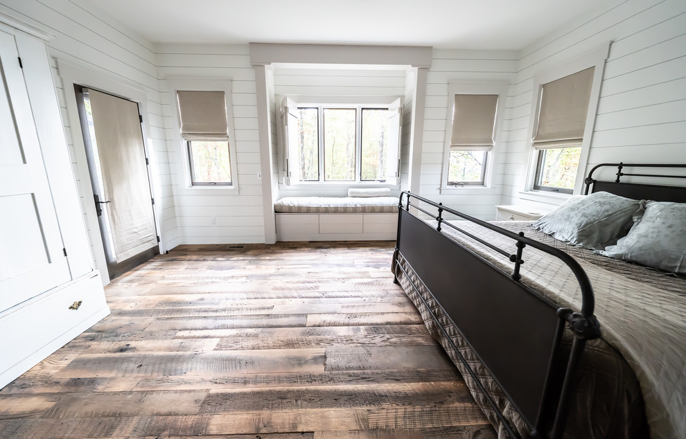 Cette image montre une chambre parentale rustique avec un mur blanc, un sol en bois brun et un sol marron.
