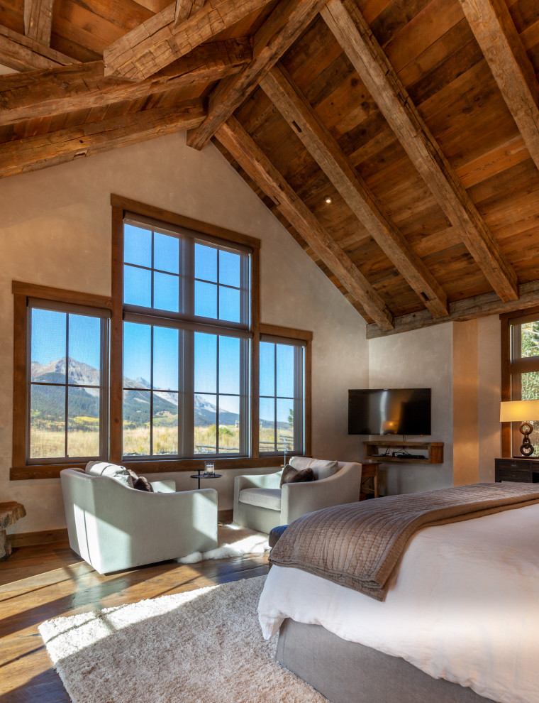 Photo of a rustic bedroom in Denver with beige walls, dark hardwood flooring, a corner fireplace, a stone fireplace surround and brown floors.