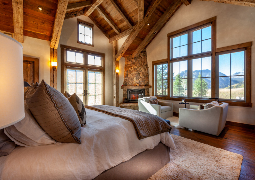 Rustikales Schlafzimmer mit beiger Wandfarbe, dunklem Holzboden, Eckkamin, Kaminumrandung aus Stein und braunem Boden in Denver