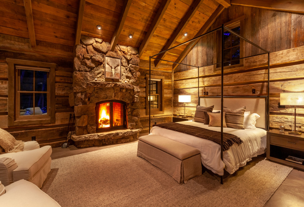 Example of a large mountain style master concrete floor and gray floor bedroom design in Denver with brown walls, a standard fireplace and a stone fireplace