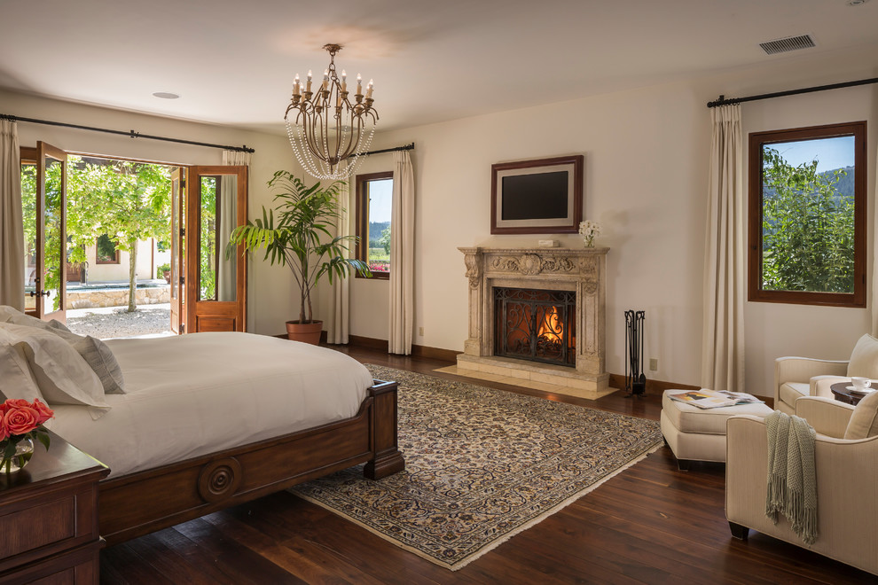 Mediterranean bedroom in San Francisco with beige walls, dark hardwood flooring, a standard fireplace and brown floors.