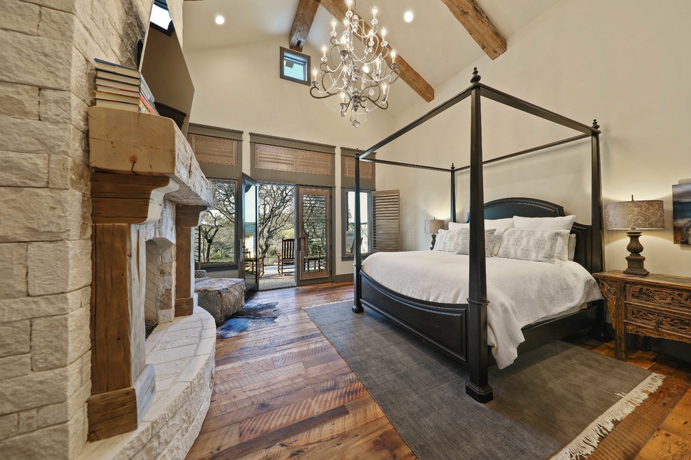 Réalisation d'une très grande chambre parentale chalet avec un mur beige, un sol en bois brun, une cheminée standard, un manteau de cheminée en pierre et un sol marron.