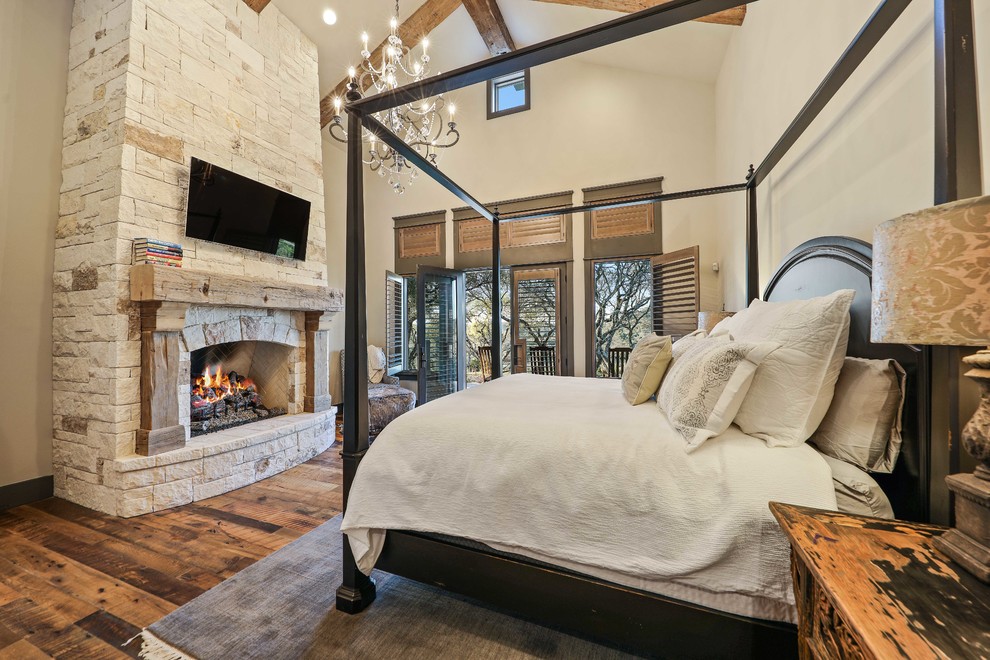 Imagen de dormitorio principal rústico extra grande con paredes beige, suelo de madera en tonos medios, todas las chimeneas, marco de chimenea de piedra y suelo marrón