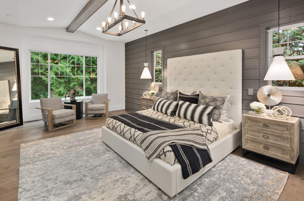 Modelo de dormitorio principal de estilo americano grande con paredes blancas, suelo de madera en tonos medios, suelo marrón, vigas vistas y panelado
