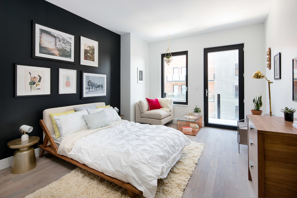 This is an example of a contemporary bedroom in New York with black walls, light hardwood flooring and no fireplace.