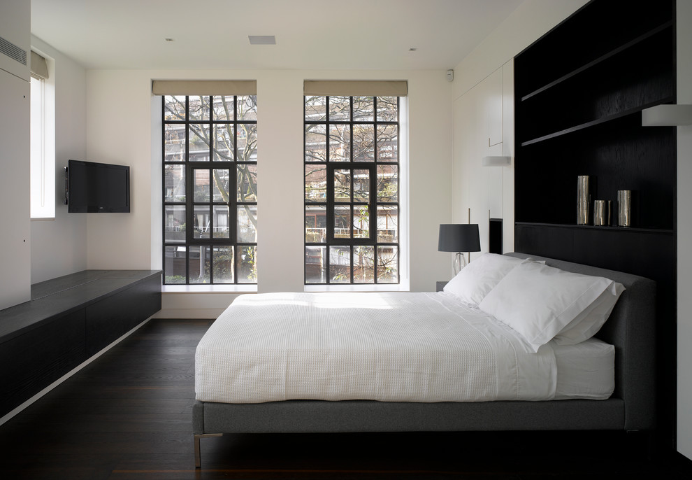 This is an example of a contemporary master bedroom in London with white walls and dark hardwood flooring.