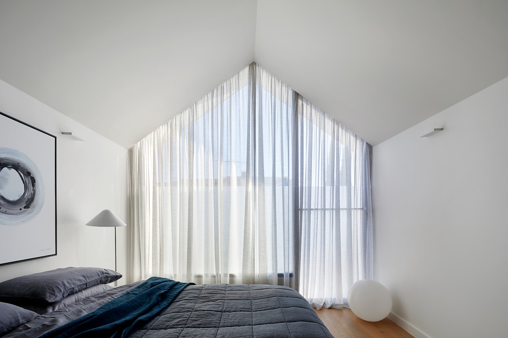 Imagen de dormitorio principal contemporáneo de tamaño medio con paredes blancas, suelo de madera clara y suelo marrón