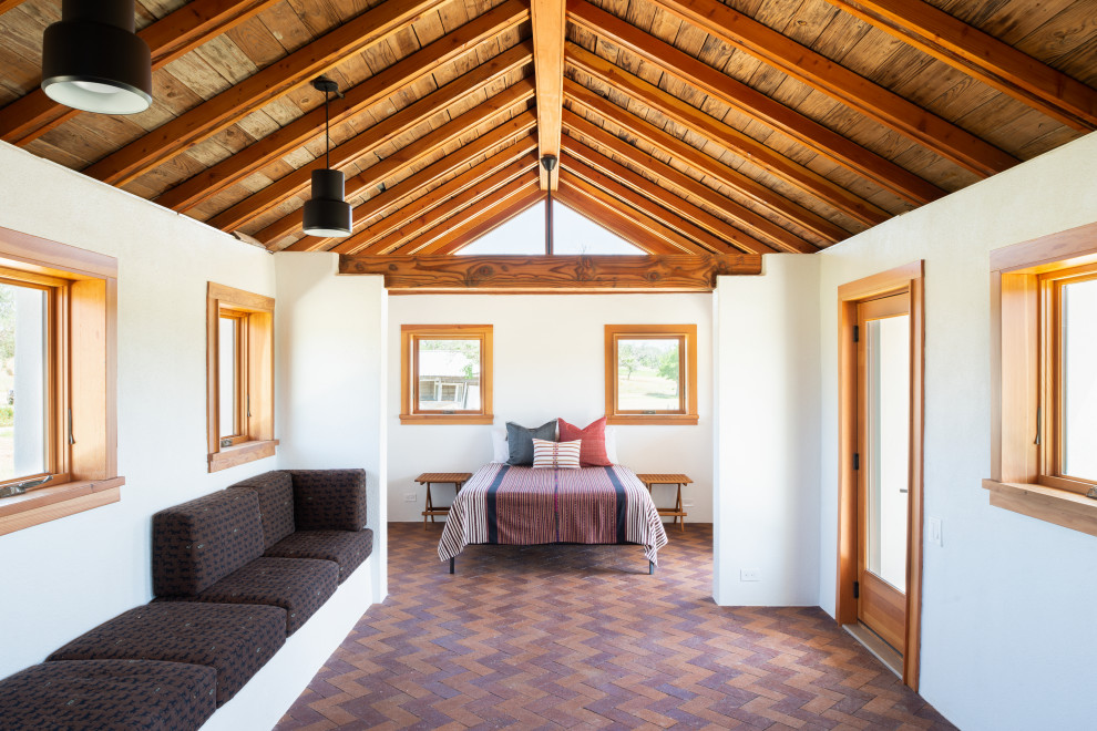 Immagine di una piccola camera matrimoniale country con pareti bianche, pavimento in mattoni, pavimento rosso e travi a vista
