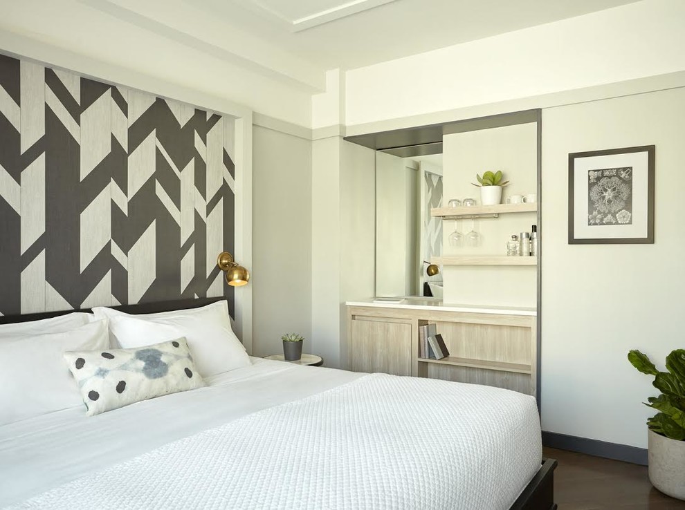 Modelo de habitación de invitados actual de tamaño medio sin chimenea con paredes beige, suelo de madera oscura y suelo marrón
