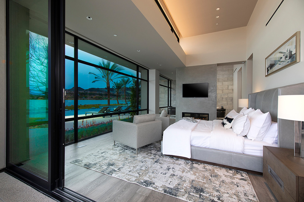 Geräumiges Modernes Hauptschlafzimmer mit grauer Wandfarbe, hellem Holzboden, Tunnelkamin, Kaminumrandung aus Beton und grauem Boden in Las Vegas