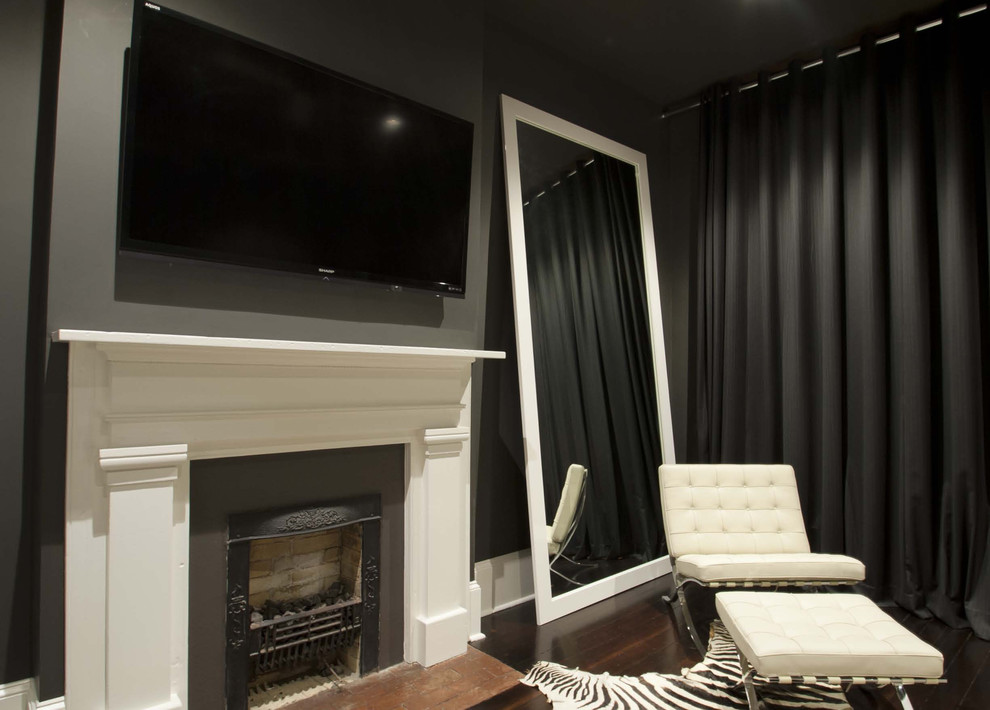 Imagen de dormitorio principal, televisión y negro actual grande con todas las chimeneas, paredes grises, suelo de madera oscura, suelo marrón y marco de chimenea de yeso