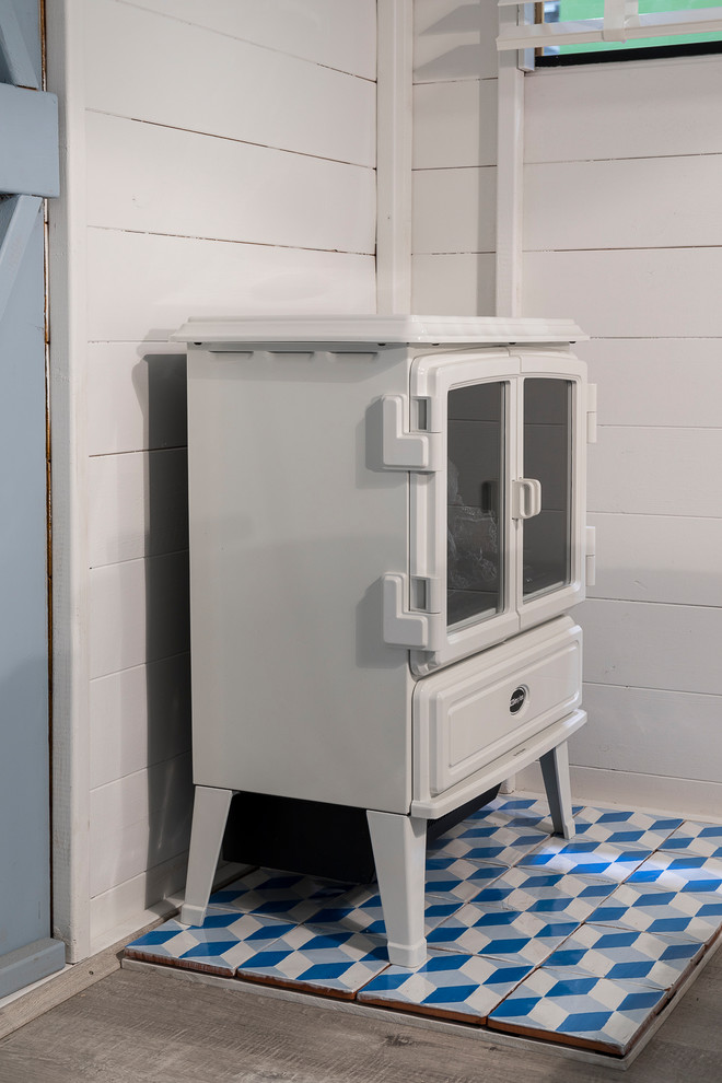 На фото: маленькая гостевая спальня (комната для гостей) в скандинавском стиле с белыми стенами, полом из ламината, печью-буржуйкой и серым полом для на участке и в саду с