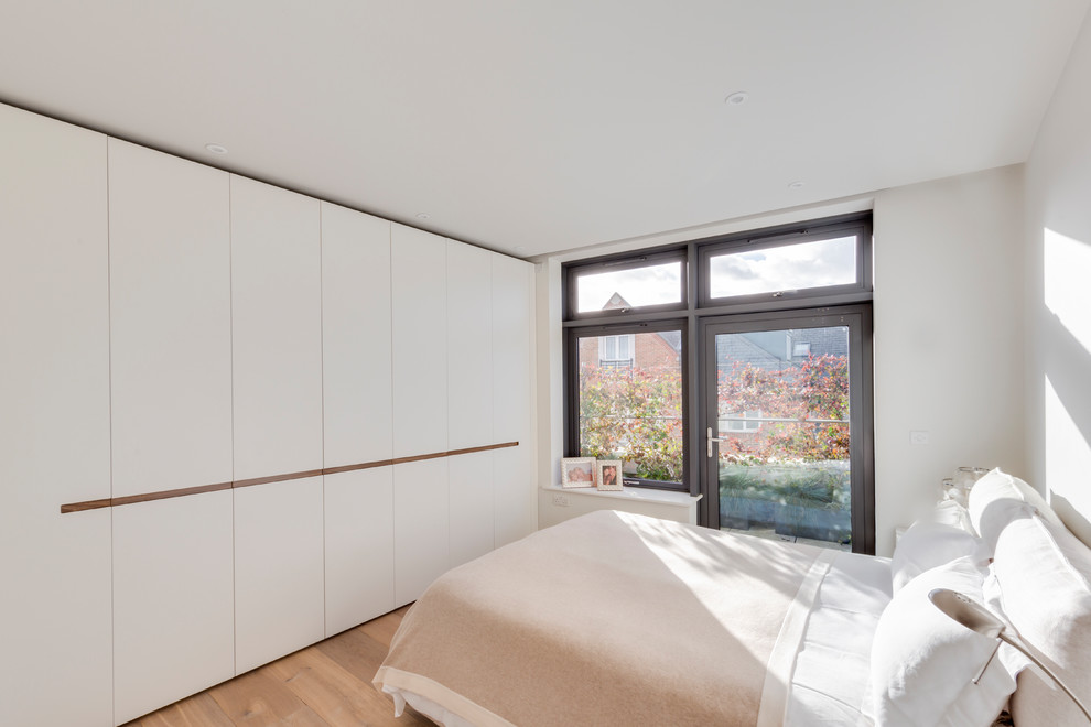 Modernes Gästezimmer mit weißer Wandfarbe, braunem Holzboden und beigem Boden in London