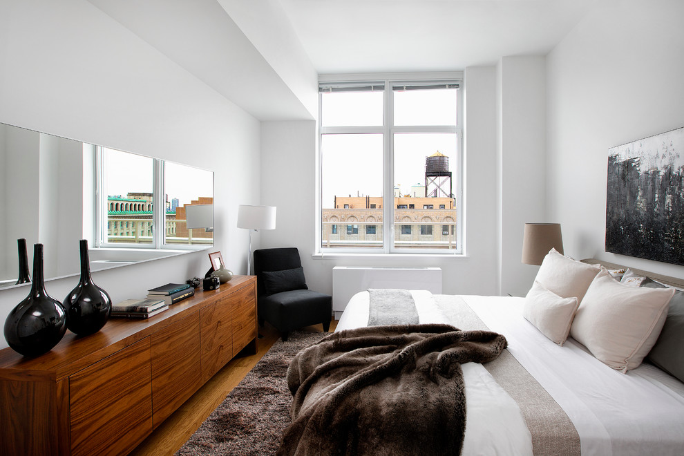 This is an example of a contemporary bedroom in New York with white walls and medium hardwood flooring.