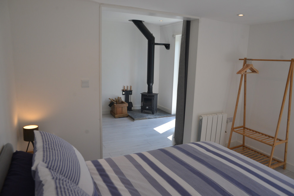 Immagine di una piccola camera degli ospiti minimal con pareti bianche, pavimento in legno verniciato, stufa a legna e pavimento bianco
