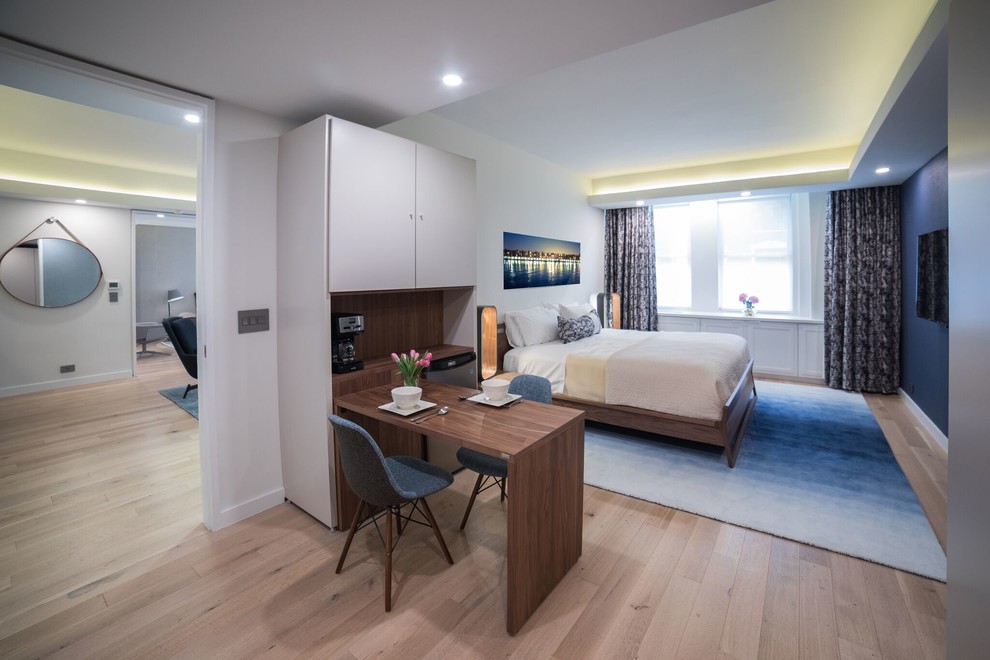 Imagen de habitación de invitados minimalista de tamaño medio sin chimenea con paredes azules, suelo de madera clara y suelo beige