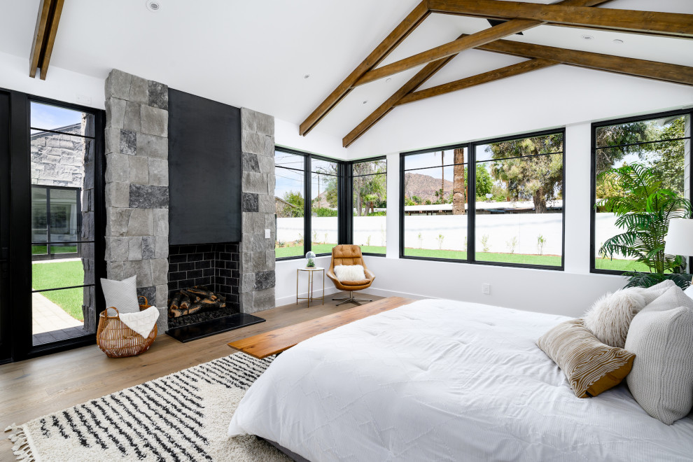 Cette photo montre une grande chambre parentale nature avec un mur blanc, un sol en bois brun, une cheminée standard, un manteau de cheminée en métal et un sol marron.