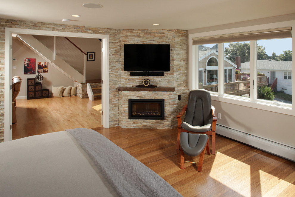 Exemple d'une chambre parentale tendance avec un mur blanc, un sol en bois brun, une cheminée d'angle et un manteau de cheminée en pierre.