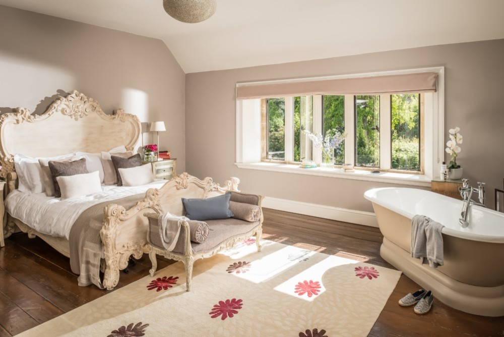 This is an example of a medium sized classic master bedroom in Dorset with beige walls, medium hardwood flooring, a stone fireplace surround and brown floors.