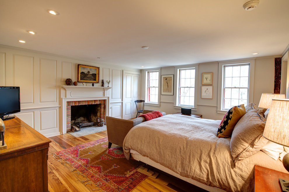 Modelo de habitación de invitados de estilo de casa de campo de tamaño medio con suelo de madera clara y marco de chimenea de ladrillo