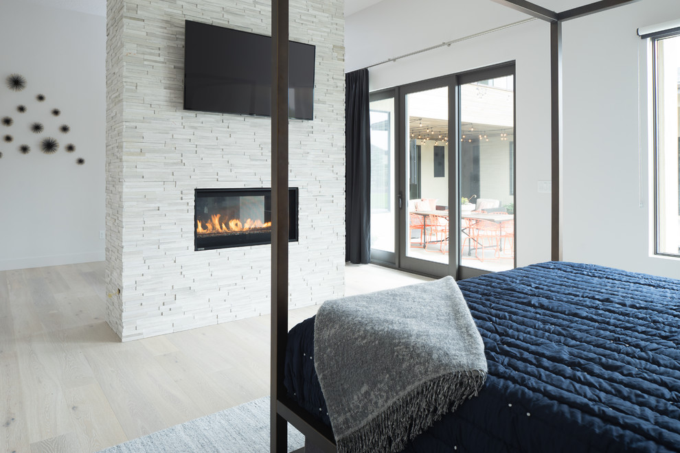 Modernes Schlafzimmer mit hellem Holzboden, Tunnelkamin und Kaminumrandung aus Stein in Boise