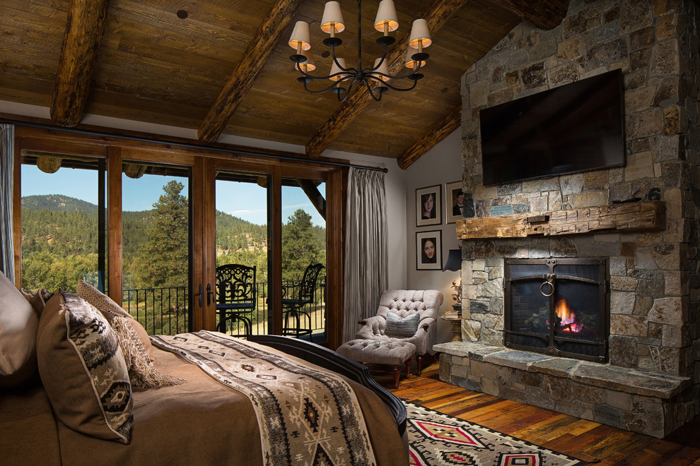 Large mountain style master dark wood floor bedroom photo in Other with gray walls, a ribbon fireplace and a stone fireplace