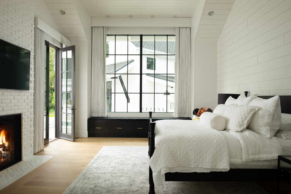 Imagen de dormitorio abovedado campestre con paredes blancas, suelo de madera en tonos medios, todas las chimeneas, marco de chimenea de ladrillo, suelo marrón y machihembrado