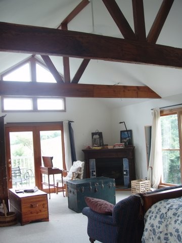 Cette image montre une grande chambre parentale rustique avec un mur blanc, une cheminée d'angle et un manteau de cheminée en bois.