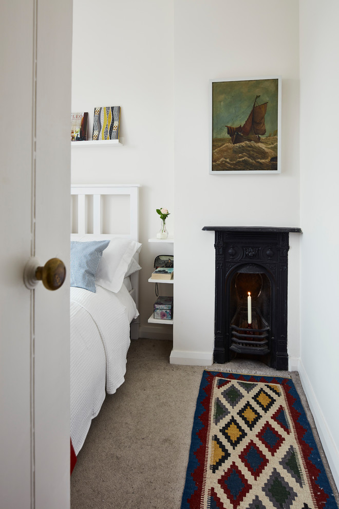 Imagen de dormitorio contemporáneo pequeño con paredes blancas, moqueta, chimenea de esquina, marco de chimenea de metal y suelo beige