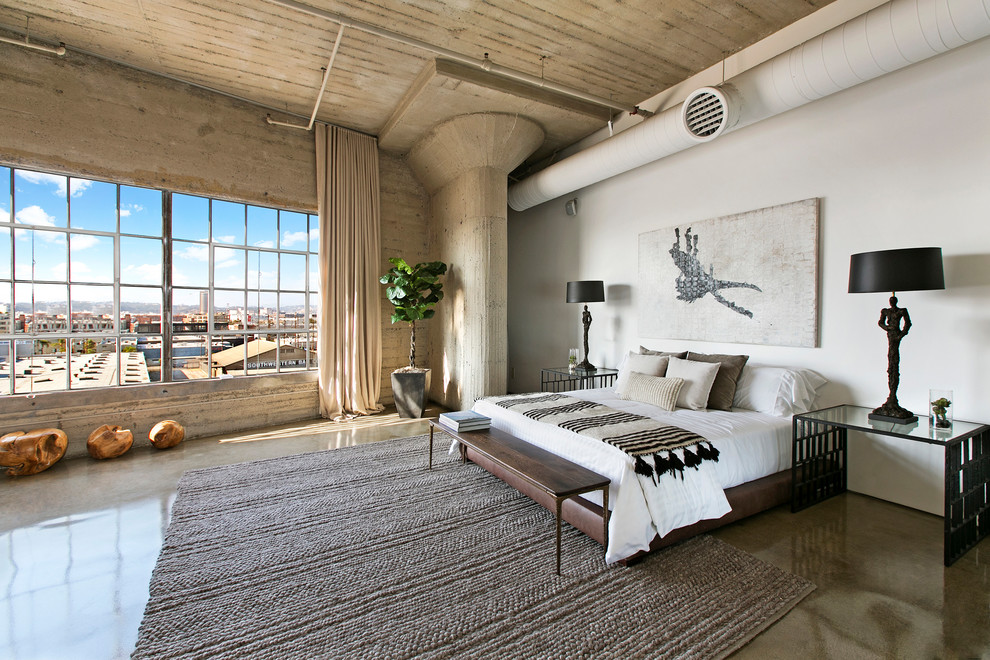 ロサンゼルスにある巨大なインダストリアルスタイルのおしゃれな寝室 (白い壁、コンクリートの床、グレーの床、ベッド下のラグ) のインテリア