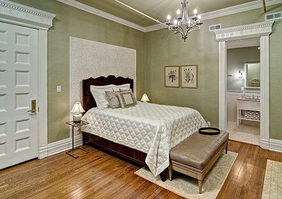 Modelo de dormitorio clásico de tamaño medio con paredes verdes, suelo de madera en tonos medios, todas las chimeneas y marco de chimenea de piedra